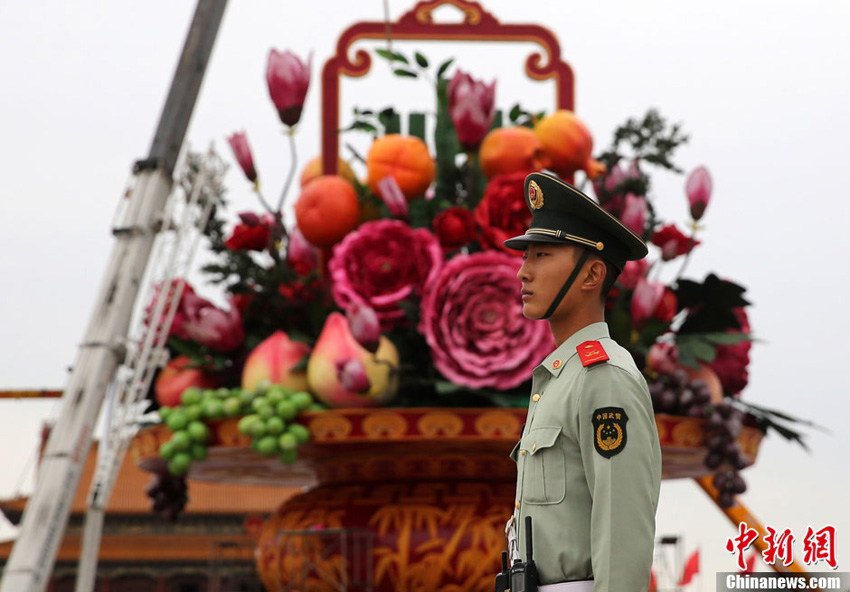 9月23日,天安门的武警走过“花果篮”。当日,北京天安门广场“祝福祖国”花坛主景“花果篮”完成主体结构安装。据了解,2013年国庆花篮高达18.2米,篮盘直径达到15米,中心花坛直径达到50米,是天安门广场历年最大的花篮。中新社发 韩海丹 摄